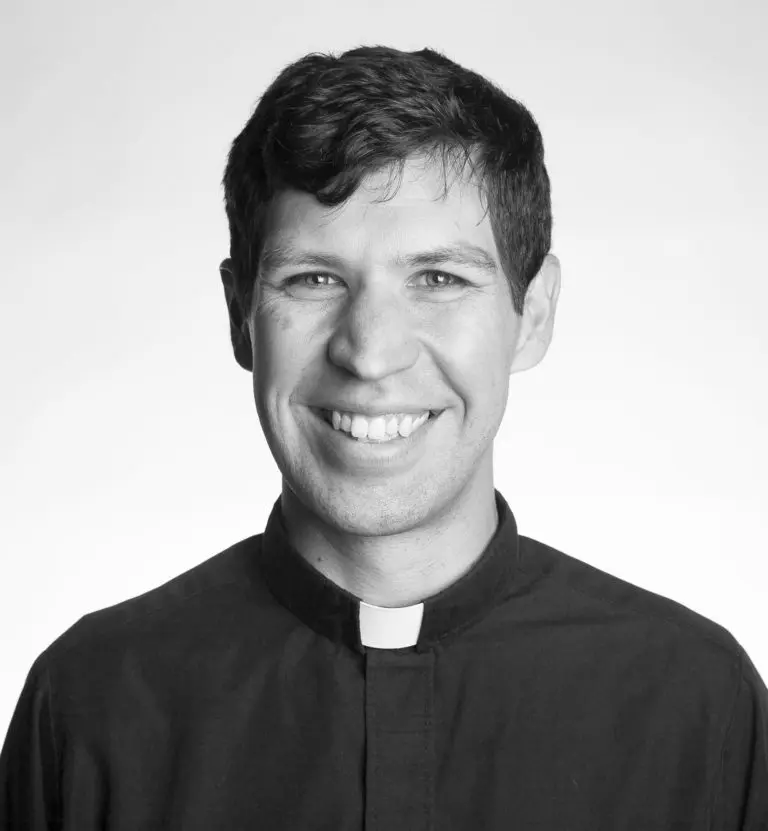 A black and white photo of a priest smiling.